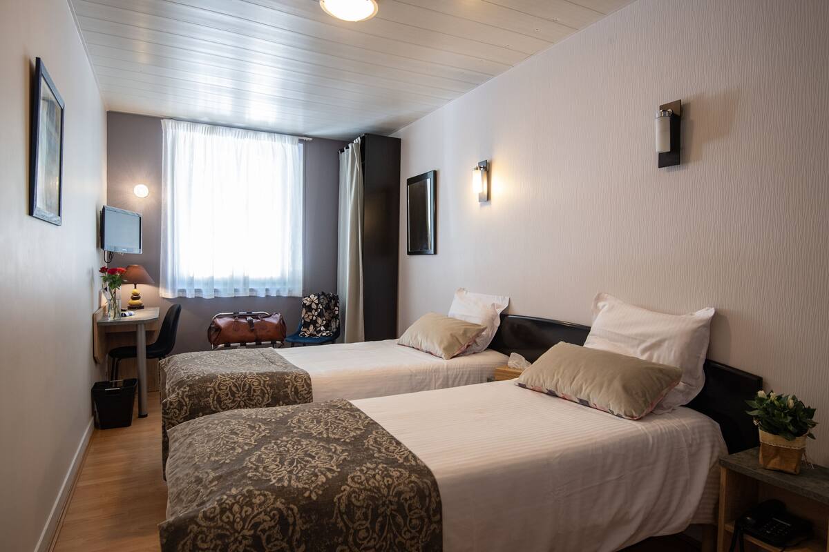 A hotel room with two beds, a desk, a chair, a small table, and a window with curtains.
