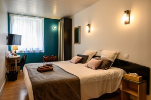 A neatly arranged hotel room with a bed, bedside table, lamp, and a desk with a chair. - Hotel Le Bayeux (Bayeux)