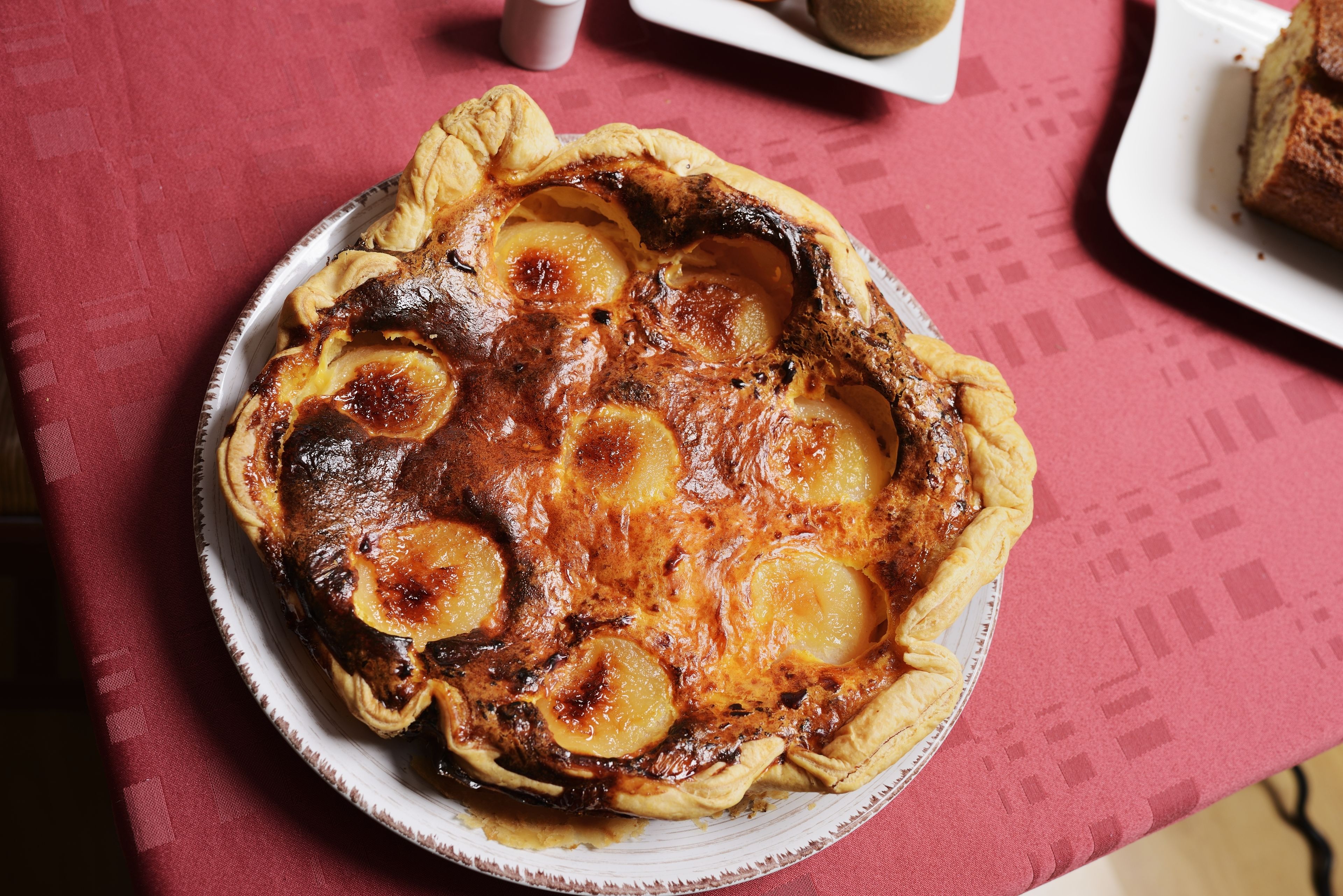 Una tarta redonda con corteza dorada y fruta caramelizada sobre un plato blanco.