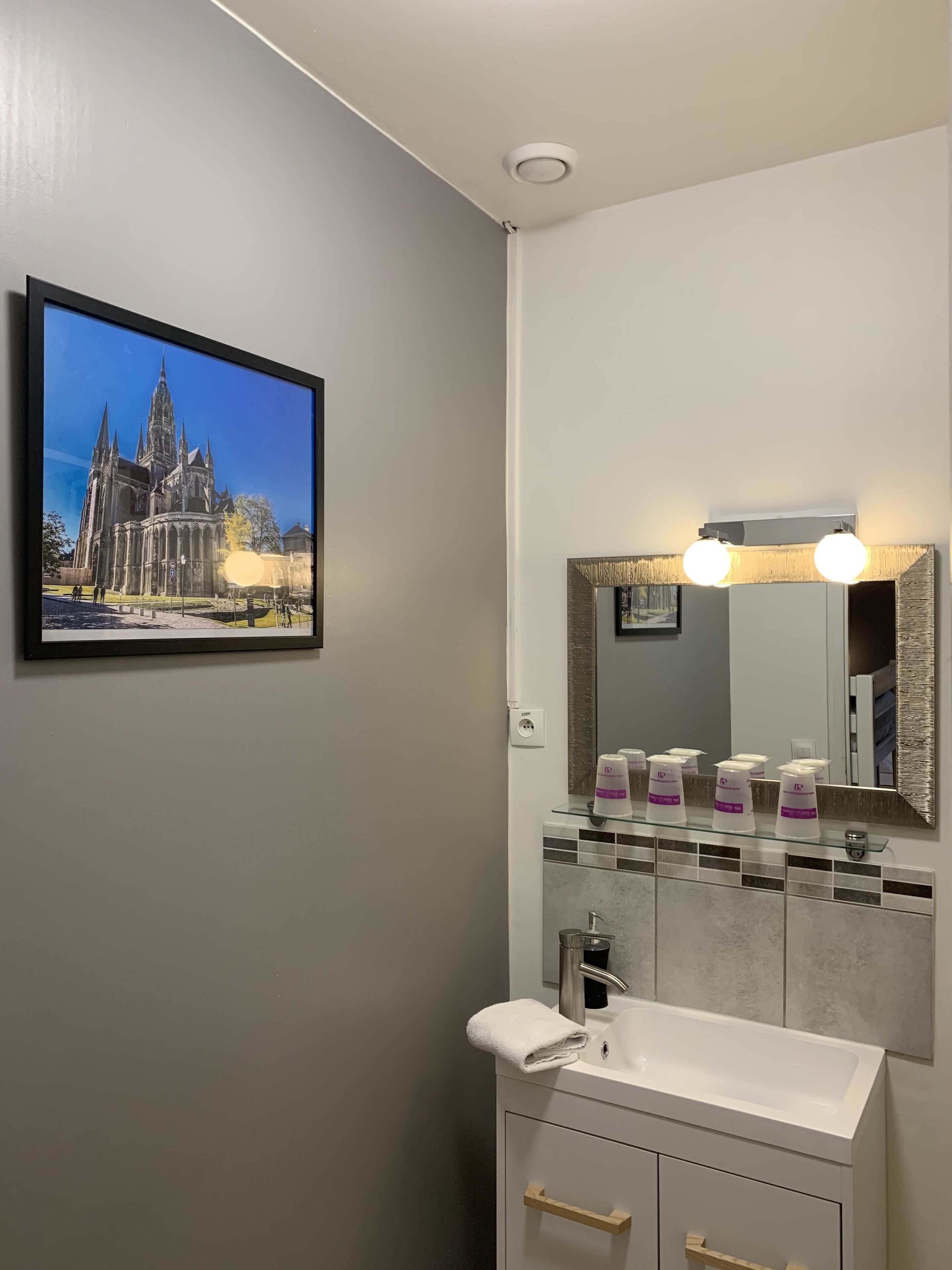 A bathroom with a large mirror, a sink, and a framed picture of a cathedral.