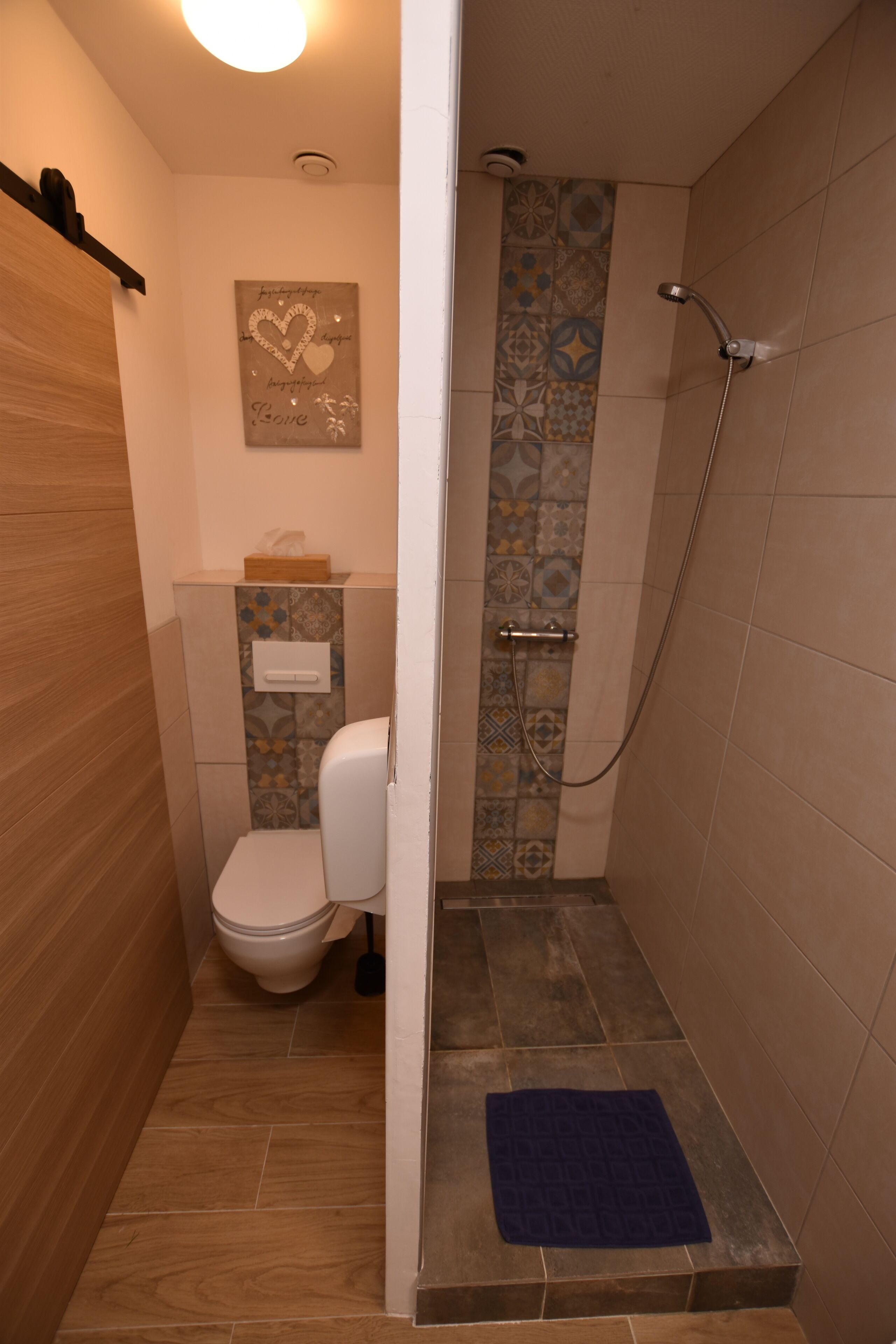 A small bathroom with a shower, toilet, and a decorative tile wall.