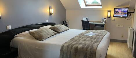 A hotel room with a large bed, a desk, a chair, a television, and a skylight.