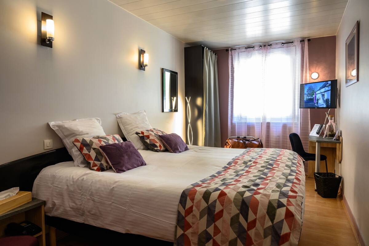 A hotel room with a large bed, a desk with a chair, a television, and a window with curtains.
