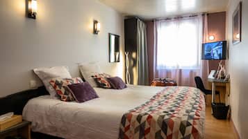 Una habitación de hotel con una cama grande, un escritorio con silla, televisión y ventana con cortinas.