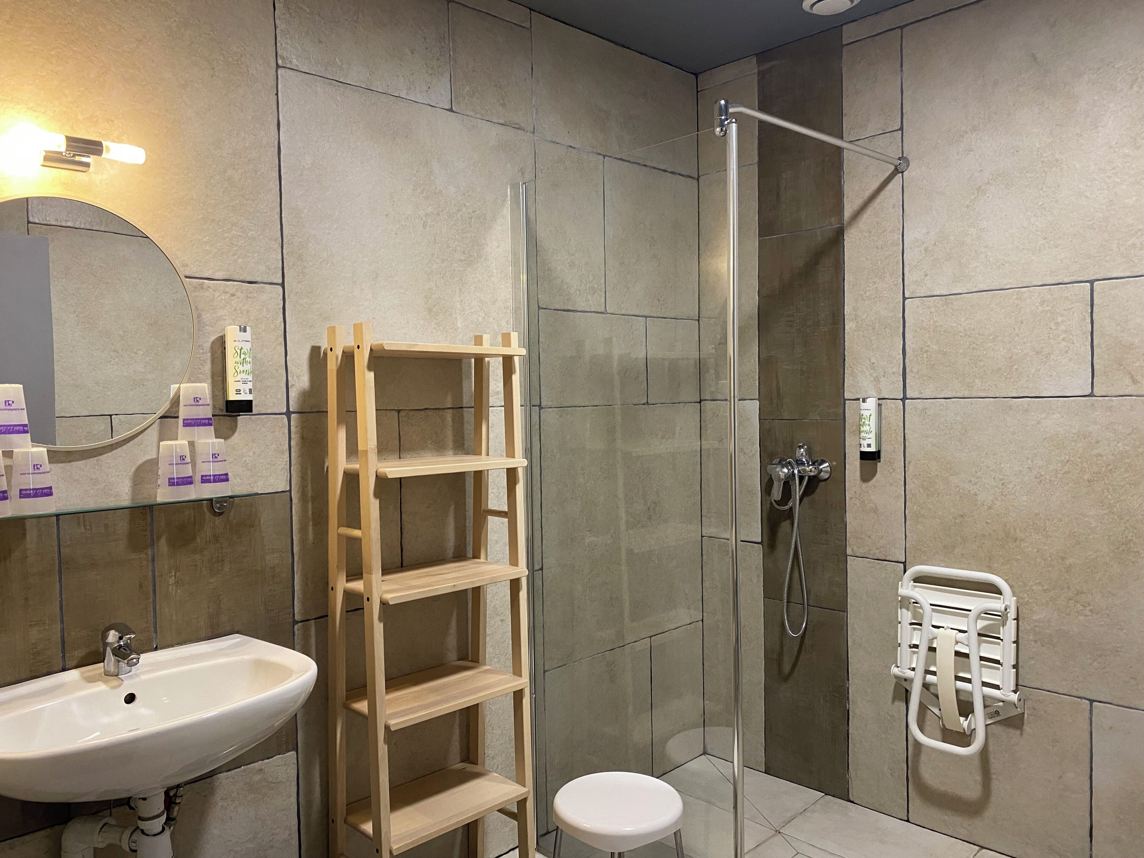 Une salle de bain équipée d’un lavabo, d’un miroir, d’une étagère en bois, d’une douche et d’un porte-serviettes.