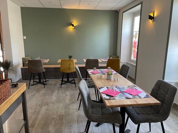 A dining area with a long wooden table, multiple chairs, and a green wall. - Hotel Le Bayeux (Bayeux)