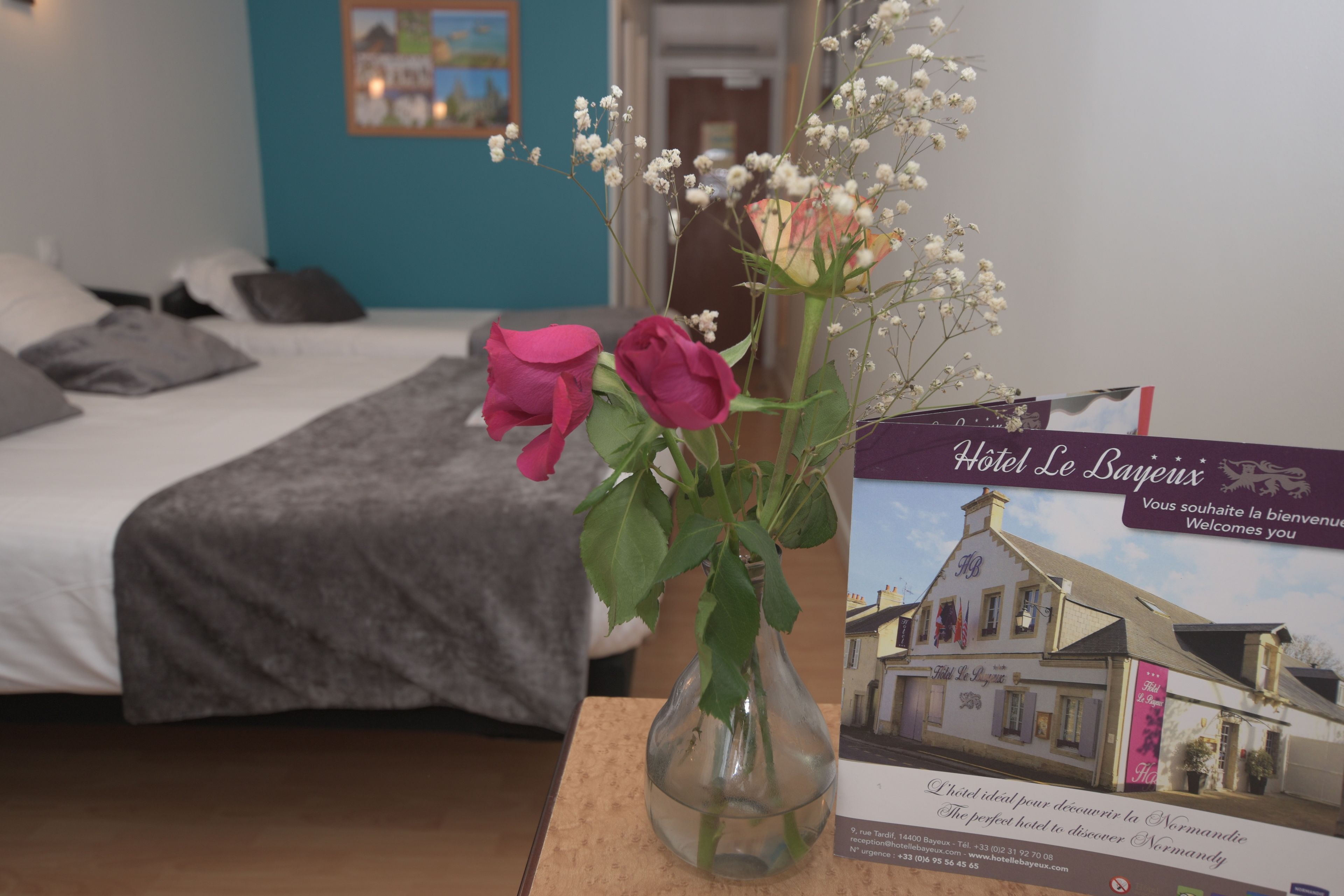 A hotel room with a bed, a vase with flowers, and a welcome sign.