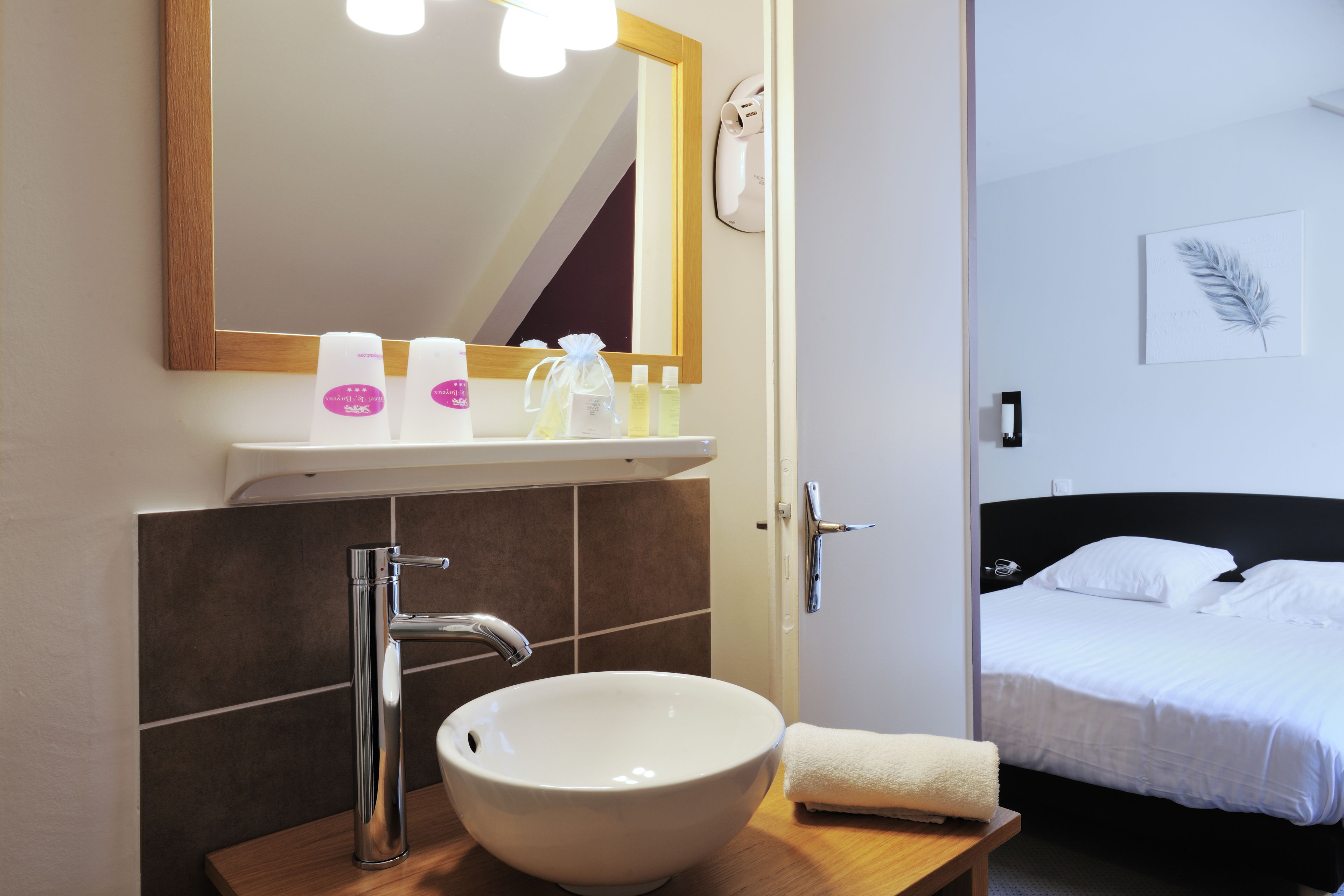 Une salle de bain avec un lavabo blanc, un miroir et des articles de toilette posés sur le comptoir.