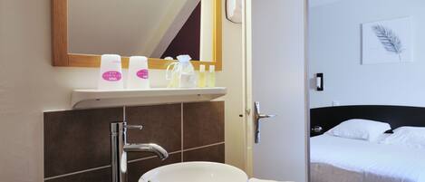Une salle de bain avec un lavabo blanc, un miroir et des articles de toilette posés sur le comptoir.