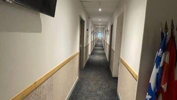 A hotel hallway with a flat-screen TV mounted on the wall, a carpeted floor, and flags on the right side.