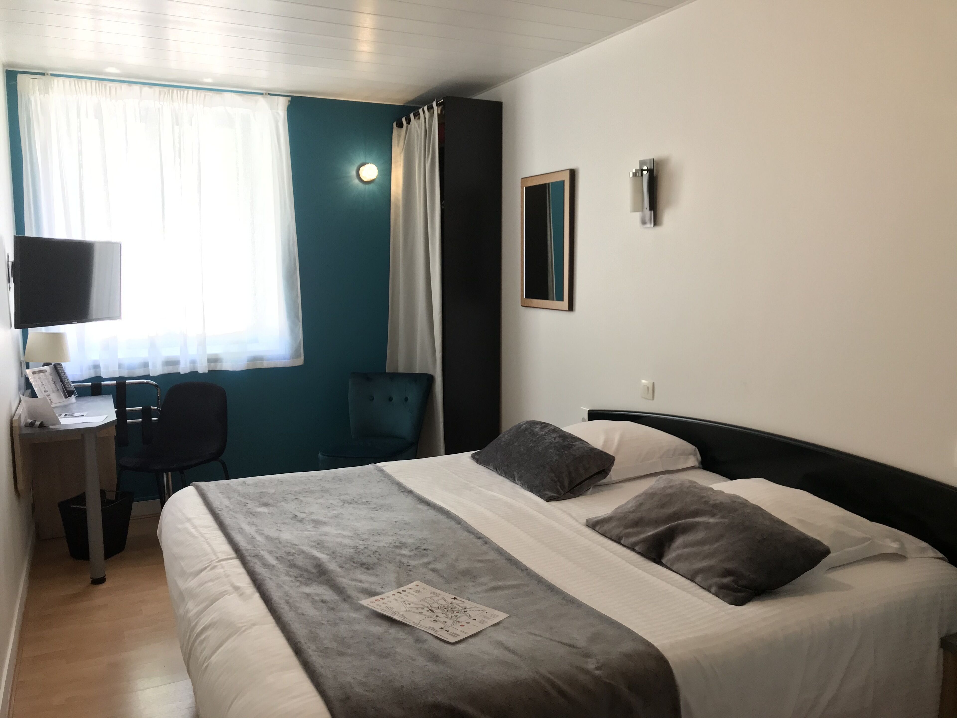 Une chambre d’hôtel avec un lit, un bureau et une chaise, une télévision et une fenêtre avec des rideaux.