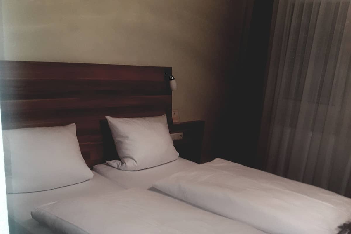 Un lit simple avec une tête de lit en bois, deux oreillers et une table de chevet avec une lampe.