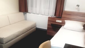 A hotel room with a bed, a sofa, a chair, a small table, and a window with curtains.