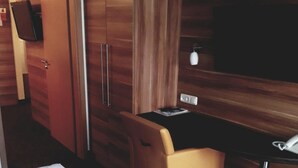 A hotel room with a bed, a desk, a chair, a wardrobe, and a television.