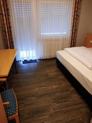 Hotellihuone, jossa on puulattia, sänky, työpöytä ja tuoli.