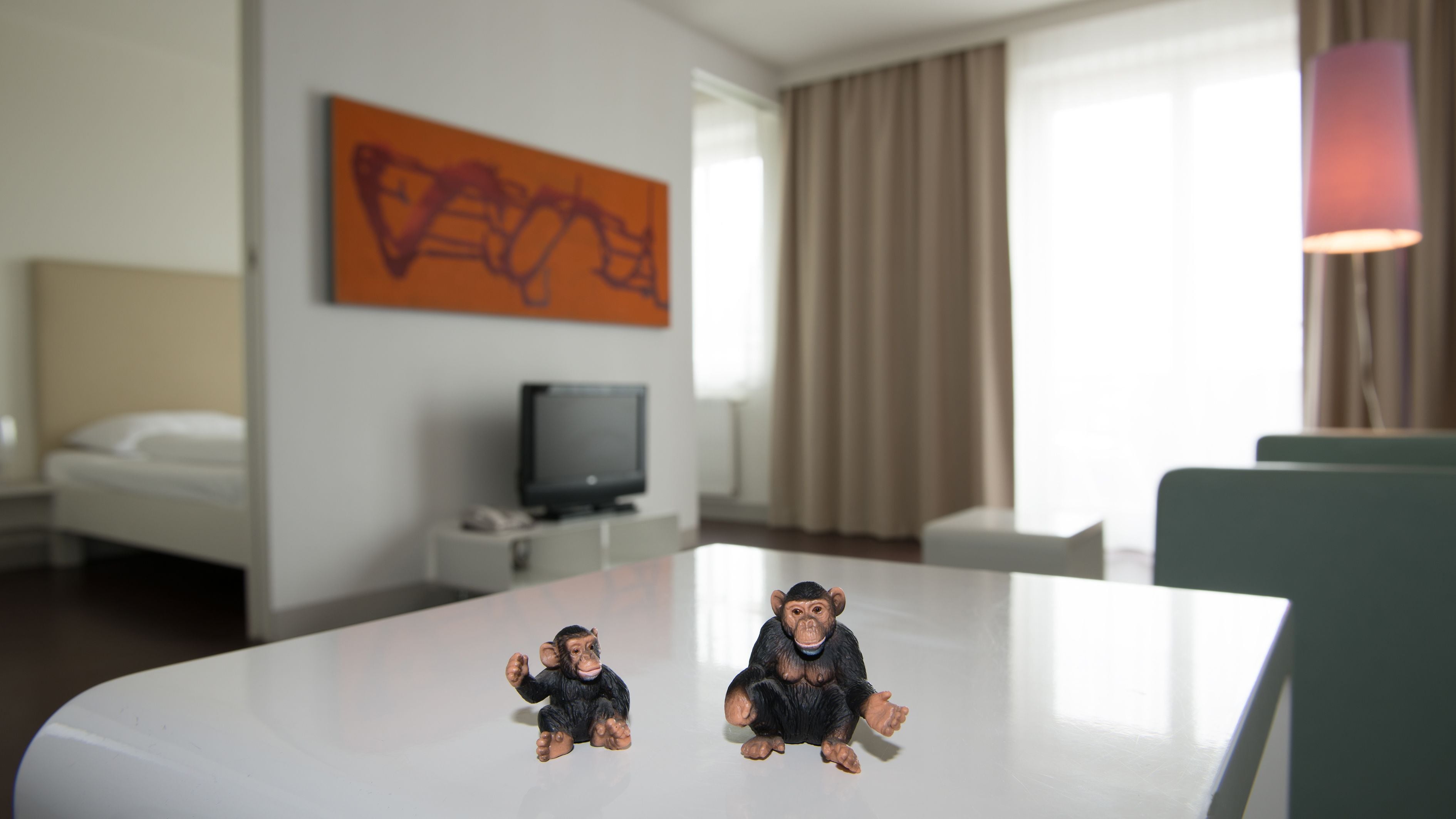 A hotel room with a bed, a television on a stand, a table with two small figurines, and a painting on the wall.