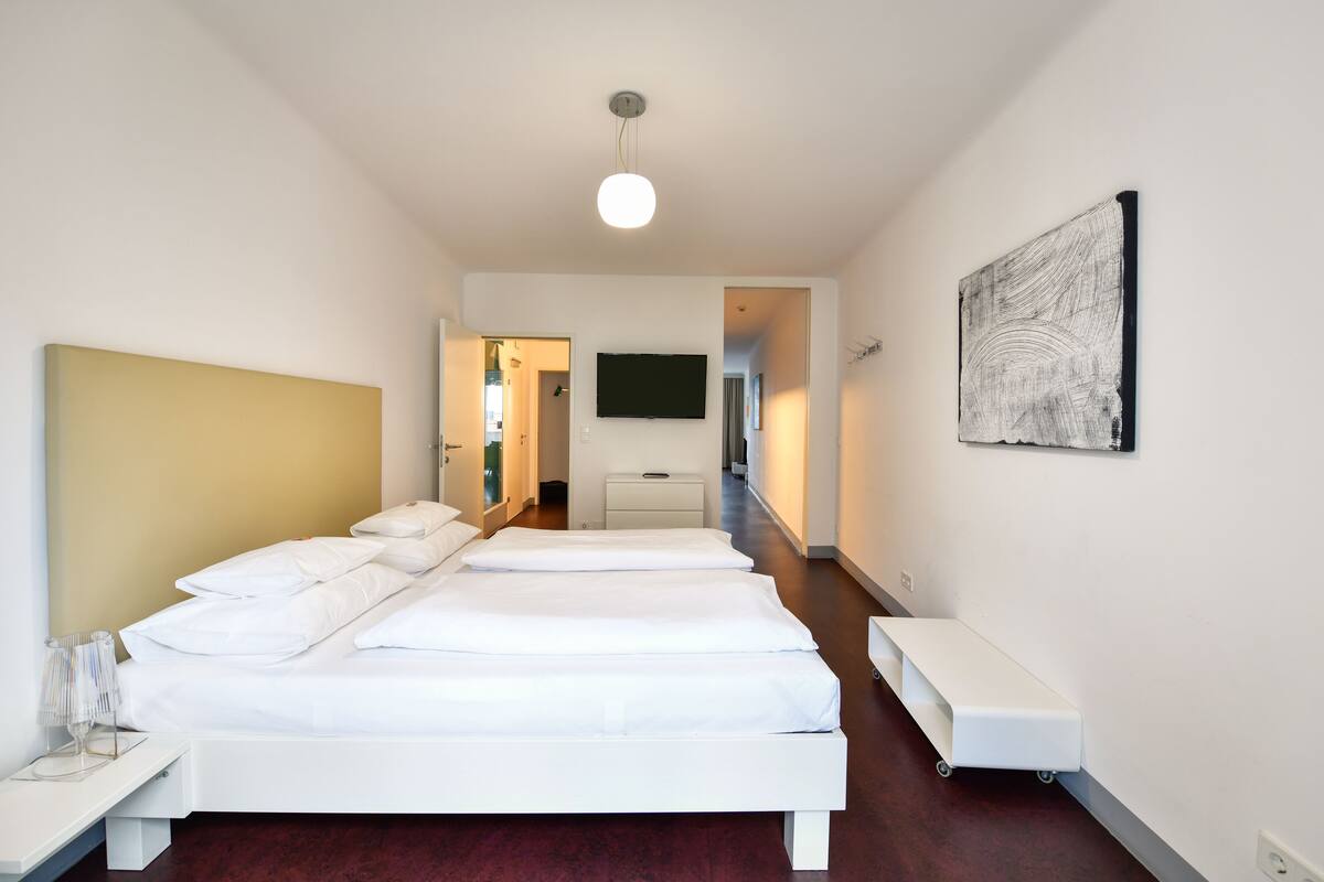 A hotel room with a large bed, a bedside table, a TV mounted on the wall, and a small desk.