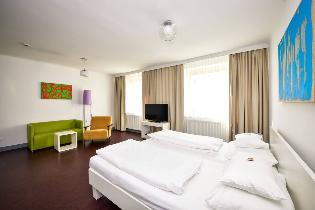 A hotel room with a large bed, a sofa, a TV, and a painting on the wall.