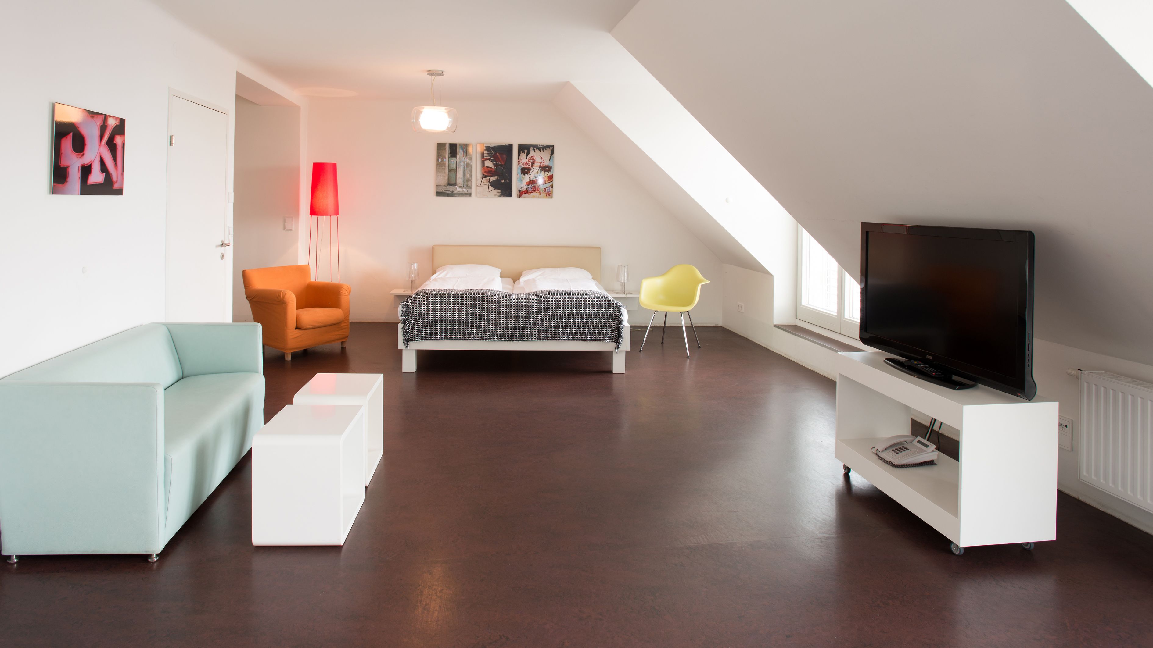 Een moderne, goed verlichte kamer met een bed, een televisie, een bank en een fauteuil.
