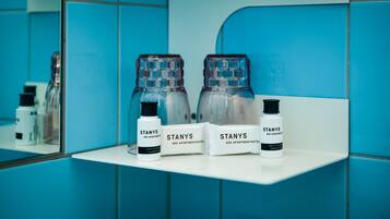 A bathroom with blue tiles and a white shelf holding three bottles of Stany's hair and body shampoo.