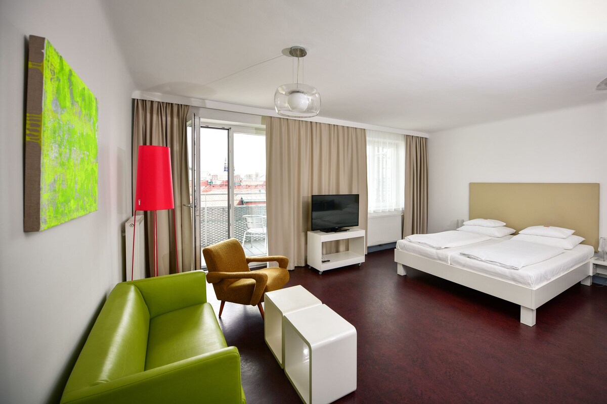 A hotel room with a bed, a TV, a sofa, a chair, and a window.