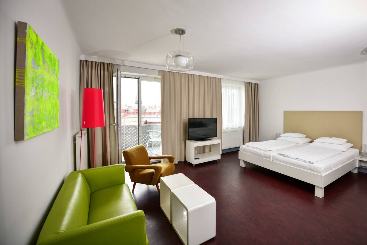 Een hotelkamer met een bed, een televisie, een bank, een stoel en een raam.