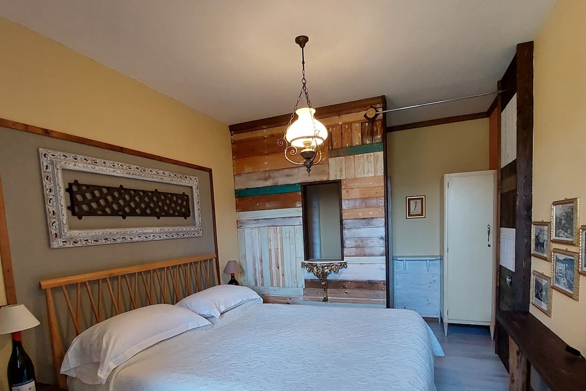 Un dormitorio con una cama grande, cabecera de madera, lámpara colgante, un espejo y un armario.