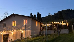Une maison dotée d’un espace extérieur couvert, d’un vignoble et, en arrière-plan, d’une colline.