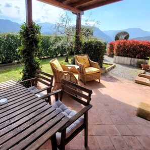 An outdoor patio with wicker furniture, a wooden table, and a view of mountains.