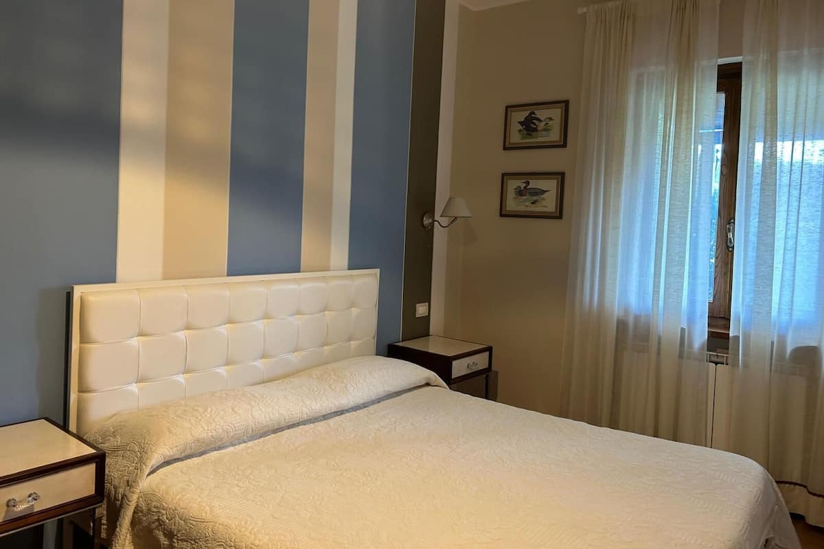 Una habitación de hotel con una cama, una mesita de noche, una lámpara y una ventana con cortinas.