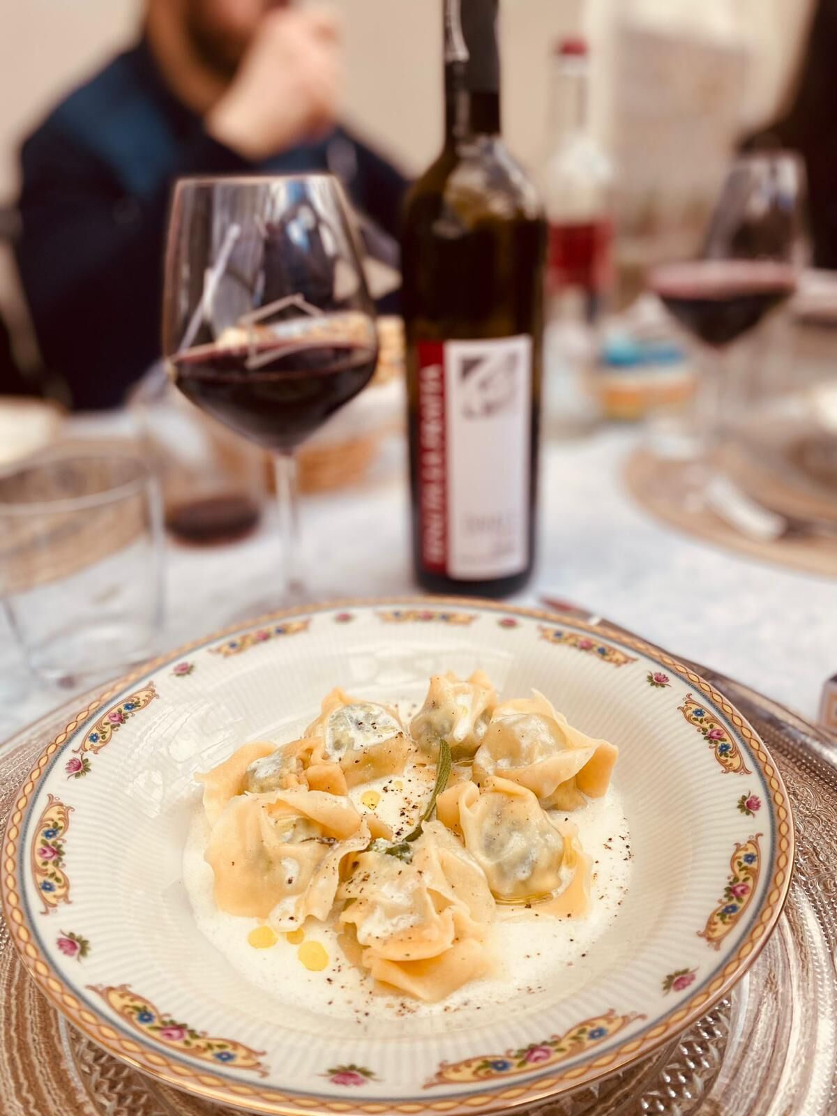 A plate of ravioli with a creamy sauce, a wine bottle, and glasses on a table.