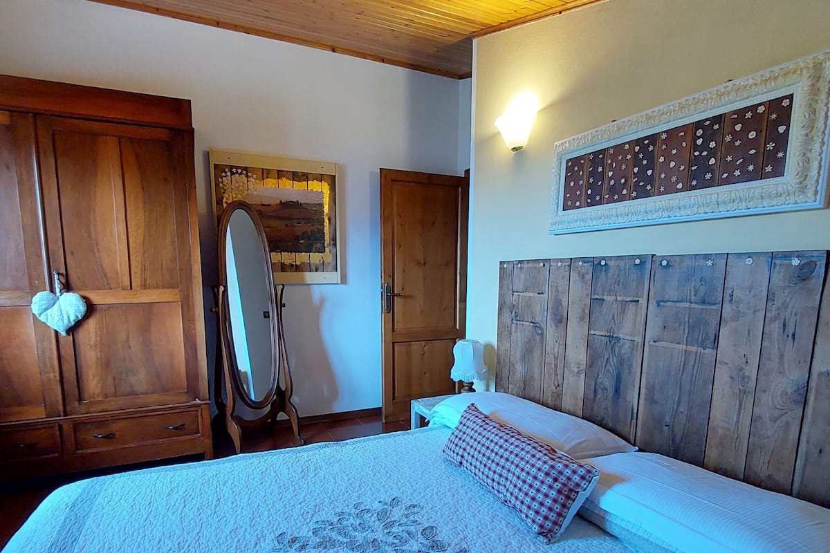 Un dormitorio con cabecera de madera, una cama grande con colcha, un espejo y una lámpara de pared.