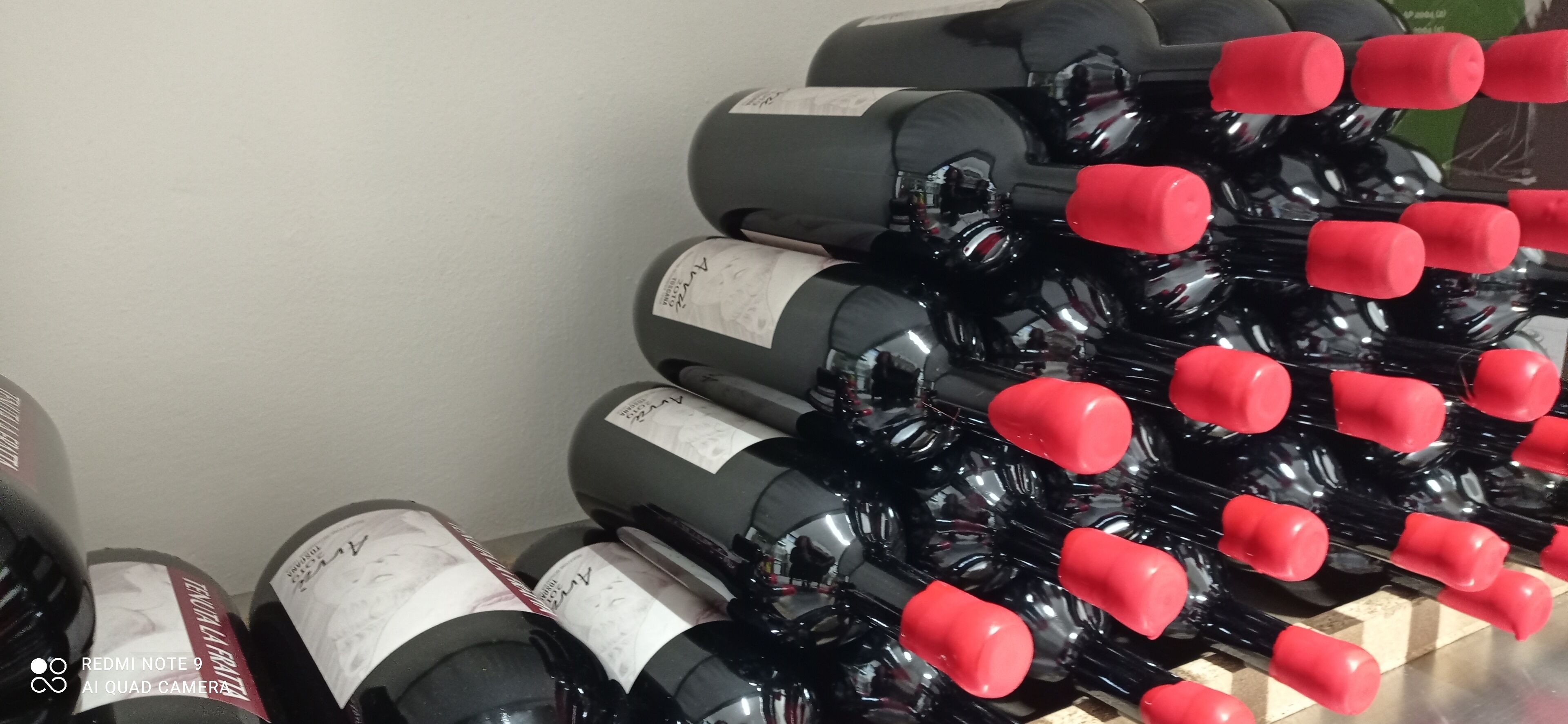 A collection of wine bottles with red caps, arranged in rows on a shelf.