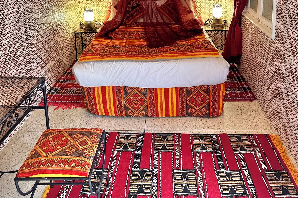 A bedroom with a bed, a hanging lamp, patterned walls, and a rug.