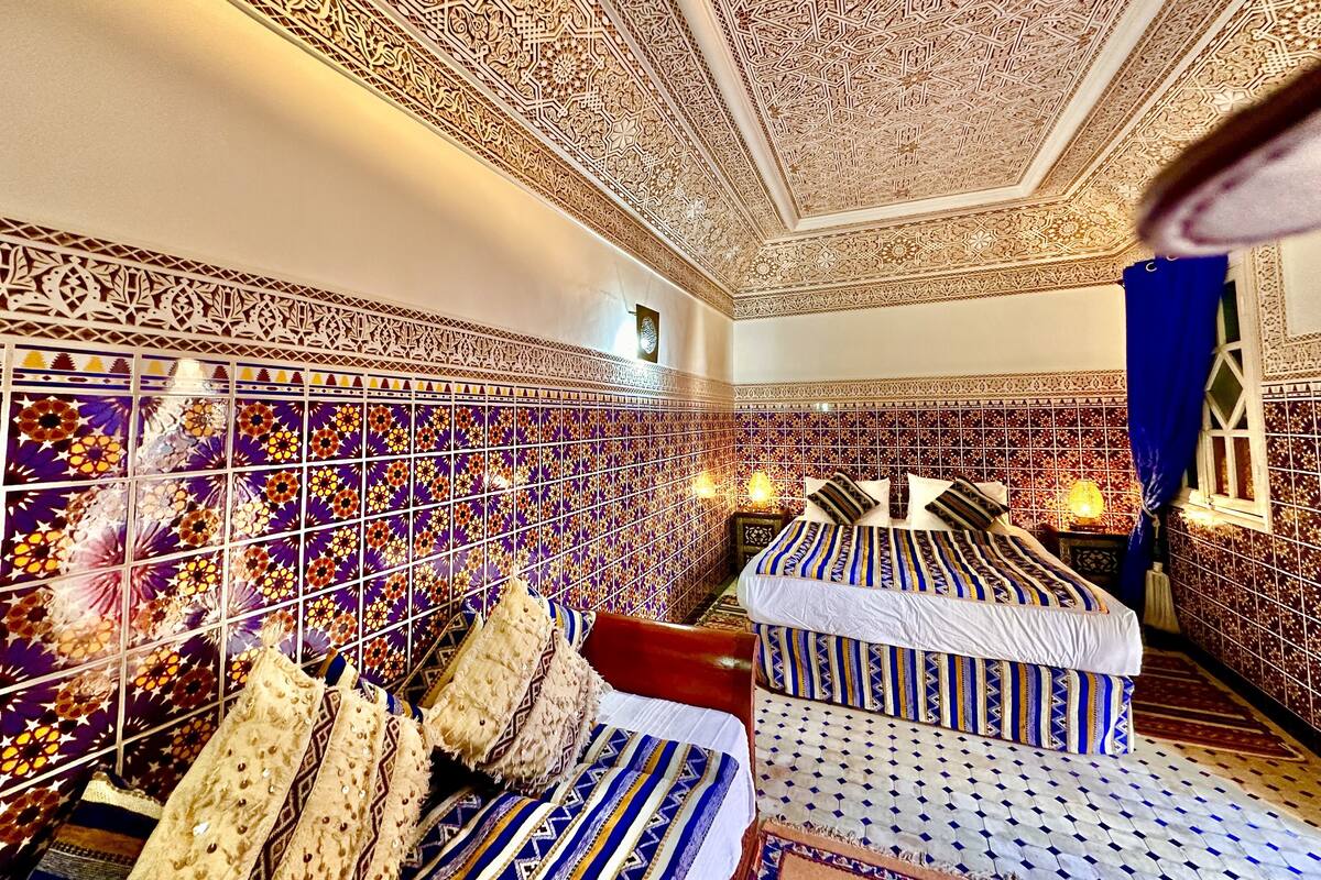 Een kamer met ingewikkelde geometrische patronen op de muren en het plafond, een bed met beddengoed met een patroon, en een decoratief wandpaneel met bloemmotieven.
