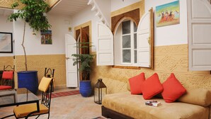 Une pièce avec un canapé beige, des coussins rouges, une plante en pot, un tonneau bleu et une petite table avec une chaise.