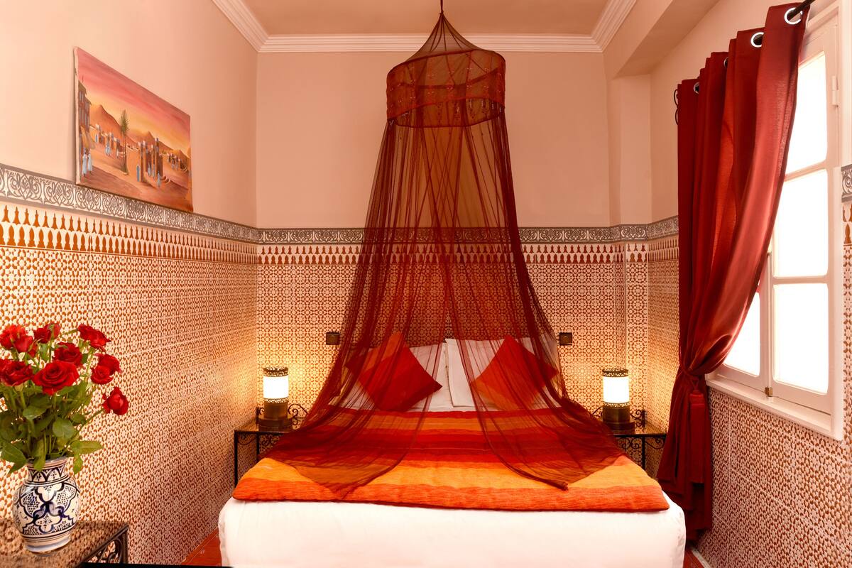 Een kamer met een bed, een nachtkastje, een vaas rode rozen en een schilderij aan de muur.
