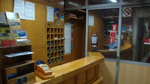 Un comptoir d’accueil avec un téléphone, un tableau d’affichage et une fenêtre sur laquelle est apposé un panneau « interdiction de fumer ».