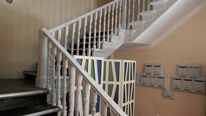 Un escalier avec des balustres blanches et une main courante, menant à un palier orné d’un panneau décoratif vert et blanc.