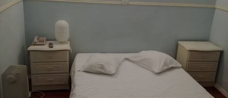 Un dormitorio con una cama, dos mesitas de noche, un radiador y una lámpara fijada a la pared.