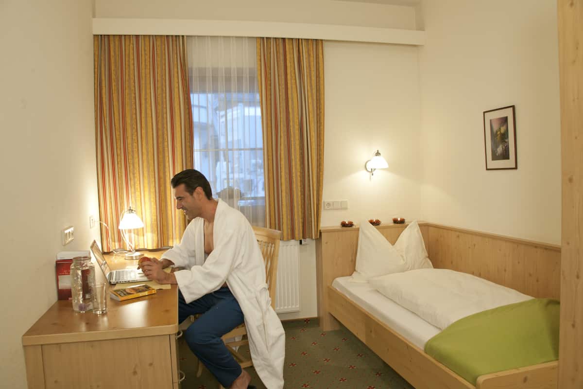 A hotel room with a wooden desk, a laptop, a lamp, a bed, and a window with curtains.