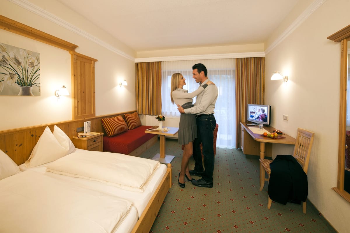A hotel room with a bed, a desk, a television, and a red sofa.