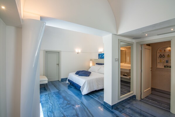 A bedroom with a bed, a bench, and a bathroom with shelves. - Grotta Palazzese (Polignano a Mare)