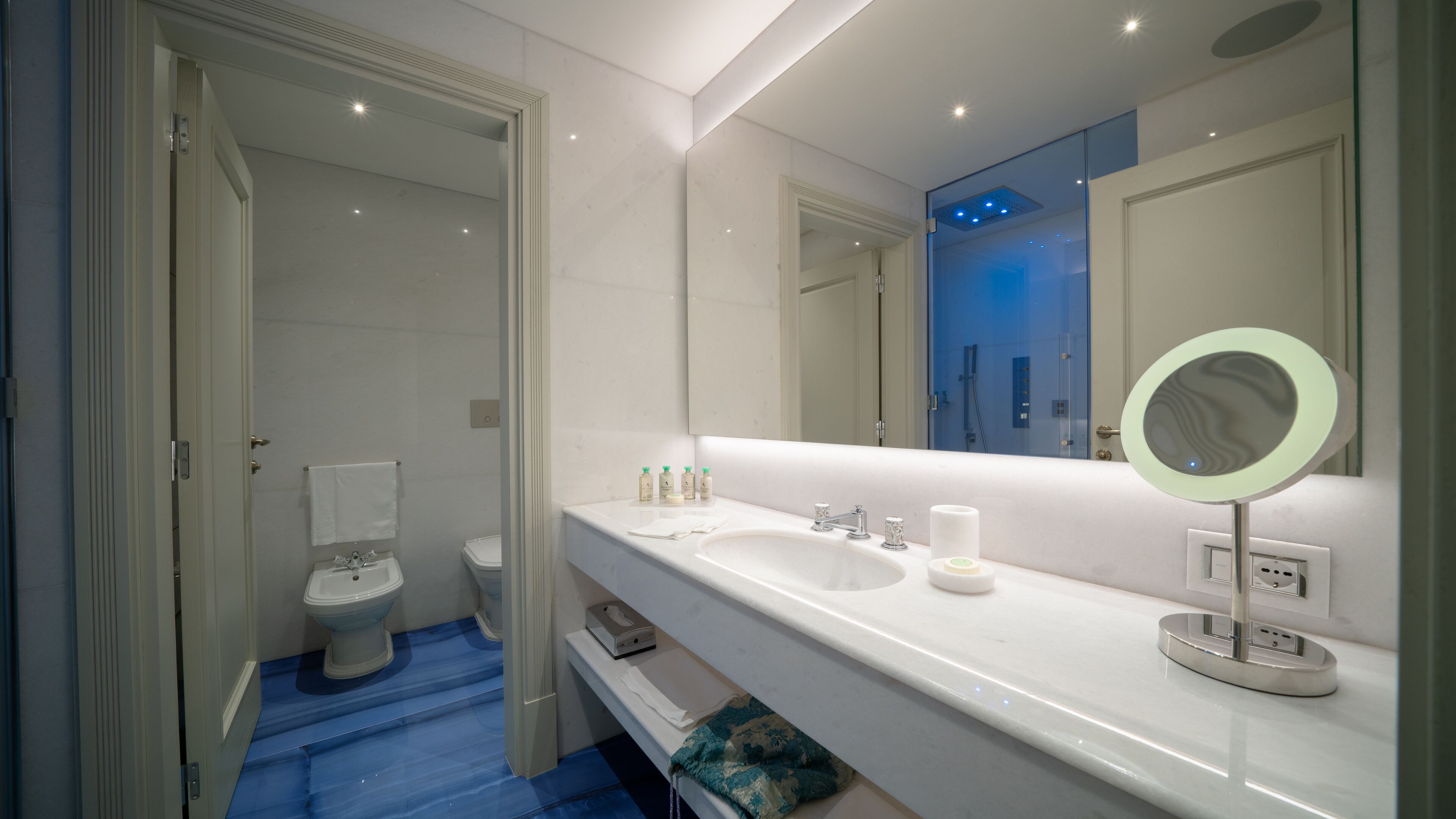 A modern bathroom with a white sink, a large mirror, and a blue shower.
