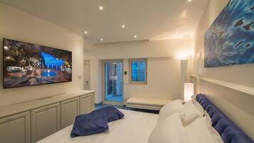 Une chambre d’hôtel moderne avec un grand lit, un téléviseur à écran plat fixé au mur, un banc et une porte donnant sur un balcon.