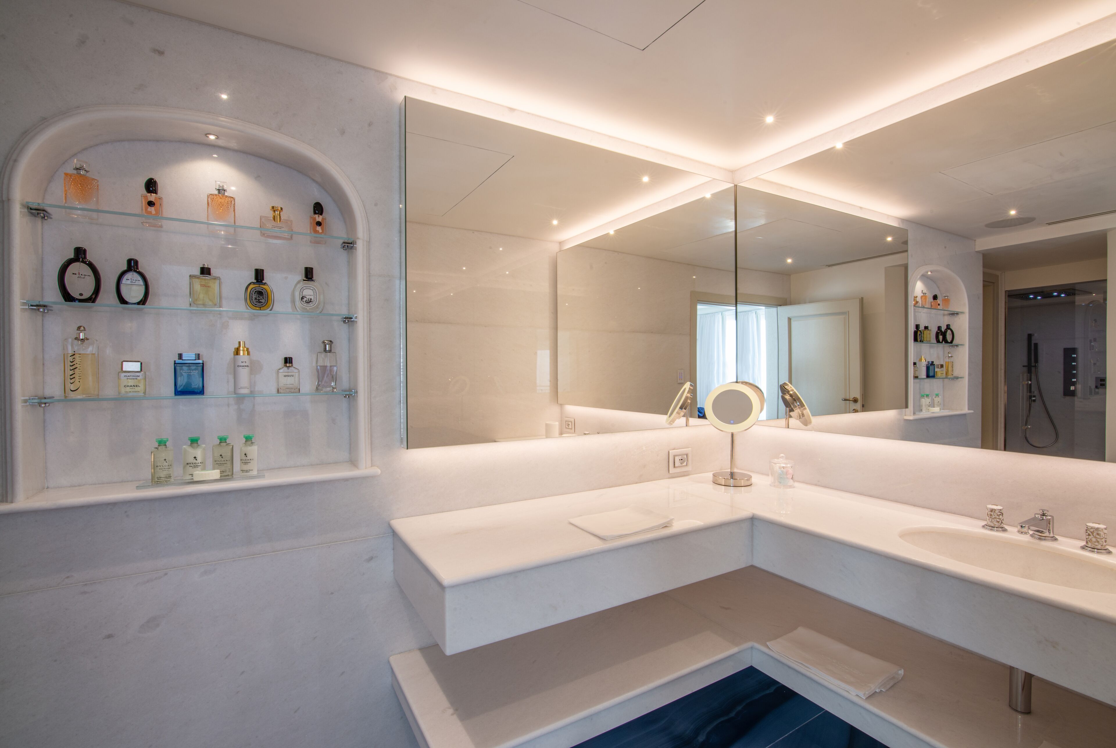 Une salle de bain moderne avec un grand miroir, un meuble-lavabo et des étagères contenant divers produits de toilette.