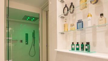 A modern bathroom with a glass shower enclosure, a marble floor, and a shelf with various toiletries.