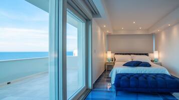 Une chambre moderne avec une grande fenêtre, un lit agrémenté d’un banc recouvert d’un tissu bleu, et des lampes de chevet.