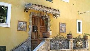 Un edificio amarillo con escaleras de piedra, una puerta de madera y barandillas decorativas de metal.