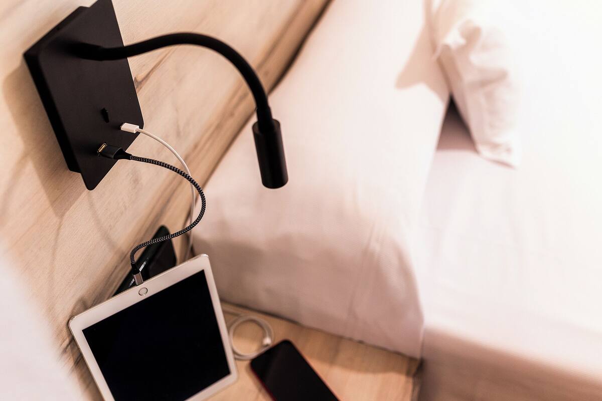 A bedside table with a tablet, a smartphone, and a black charging cable.